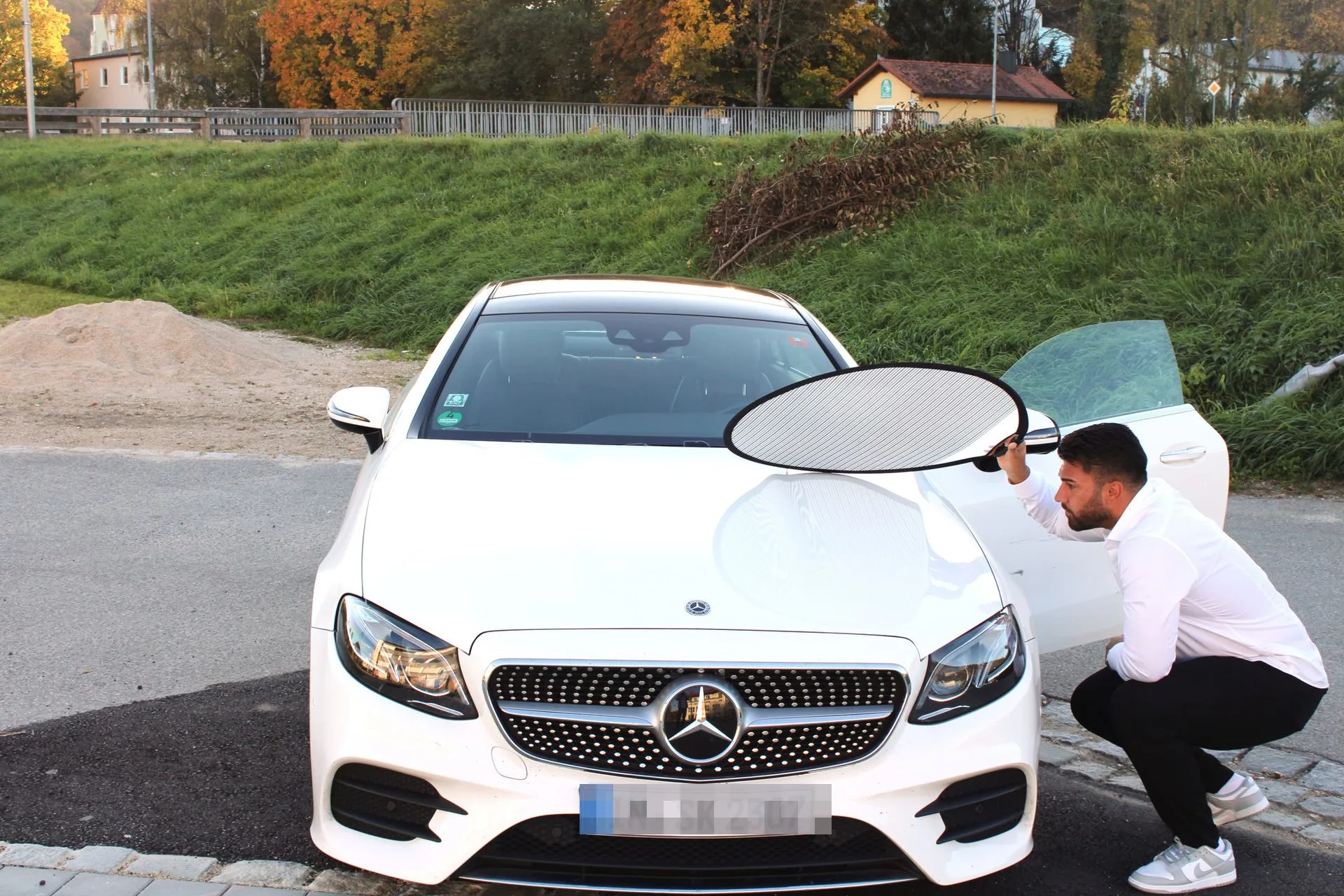 Diren Köysüren begutachtet Kratzer mit Schattenwerfer an einem weißen Mercedes